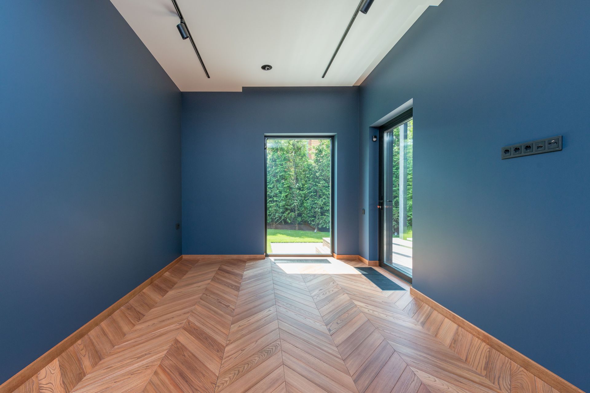 Spacious room featuring blue walls, wooden herringbone floor, and glass doors leading to a garden.