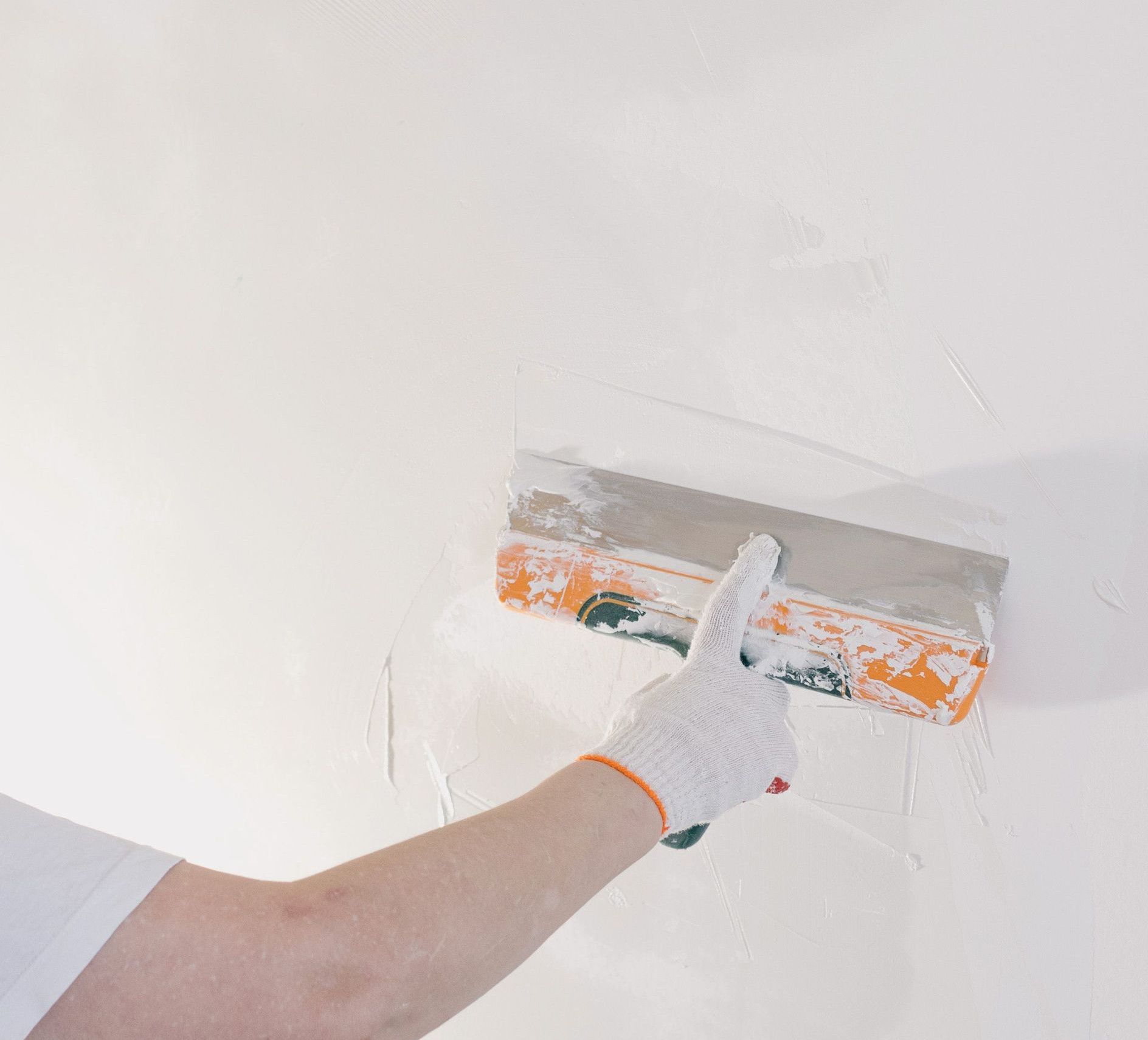 Crop anonymous male in gloves holding spatula and plastering walls in room at home