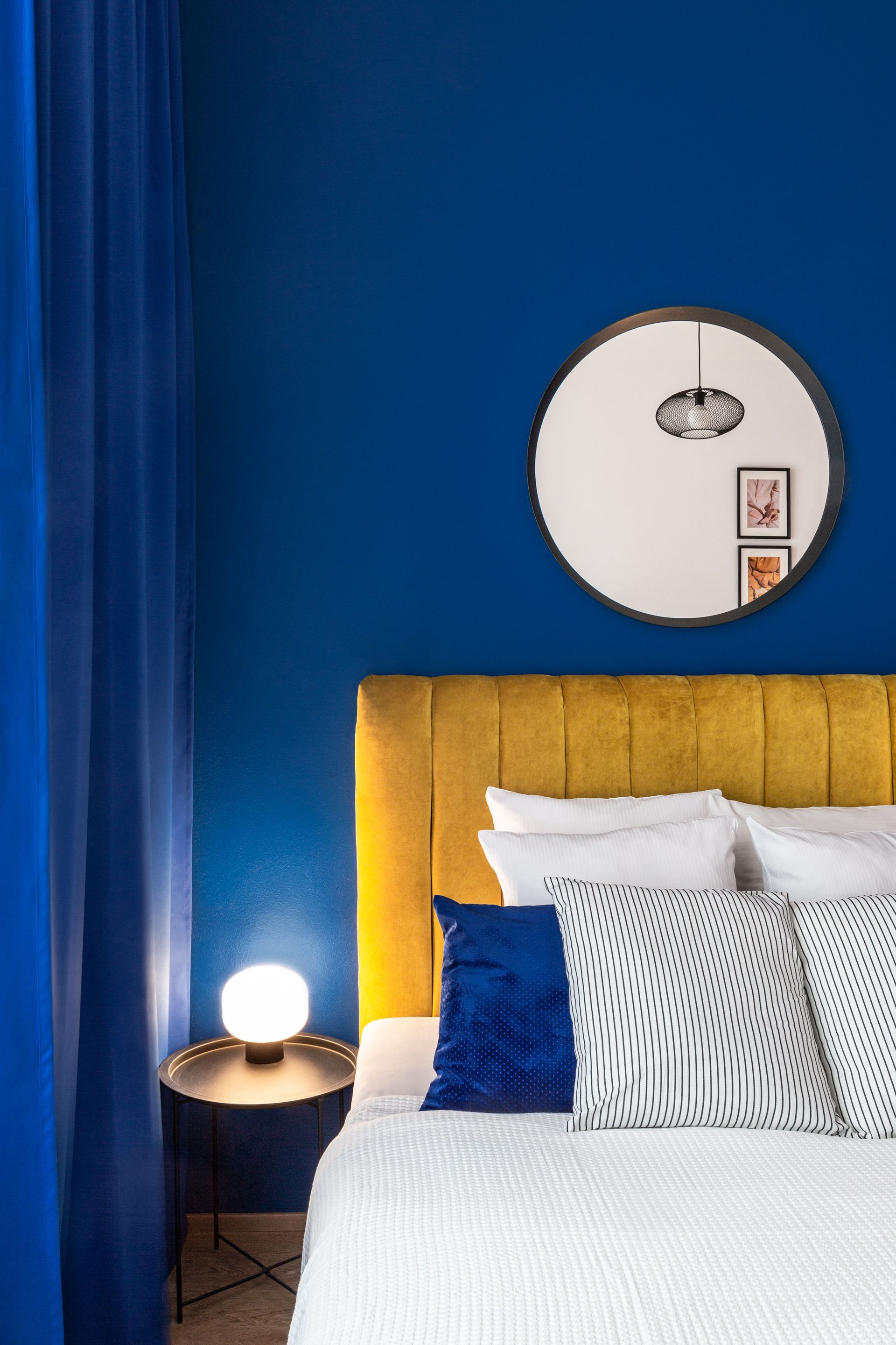 Elegant bedroom interior with blue walls, yellow headboard, and stylish decor.